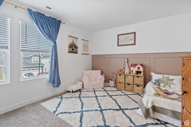 carpeted bedroom featuring wainscoting, a decorative wall, and visible vents