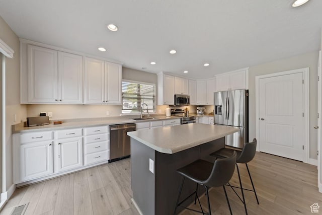 kitchen featuring light wood-style flooring, appliances with stainless steel finishes, a kitchen breakfast bar, and white cabinetry