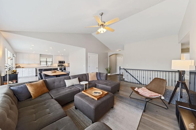 living area with arched walkways, light wood-style flooring, a ceiling fan, and high vaulted ceiling
