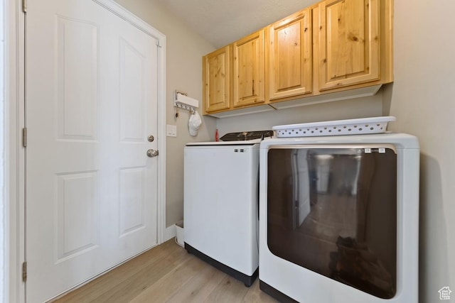 clothes washing area with washing machine and clothes dryer, light wood-style flooring, and cabinet space