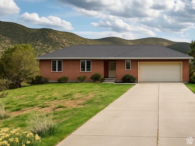single story home with a front lawn, a mountain view, brick siding, concrete driveway, and an attached garage