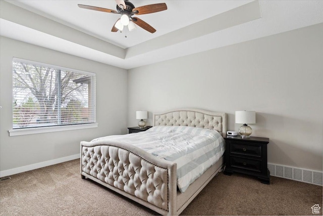 carpeted bedroom with baseboards, visible vents, a ceiling fan, and a tray ceiling