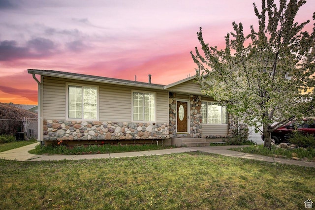 view of front of home featuring a front lawn, central AC unit, and stone siding
