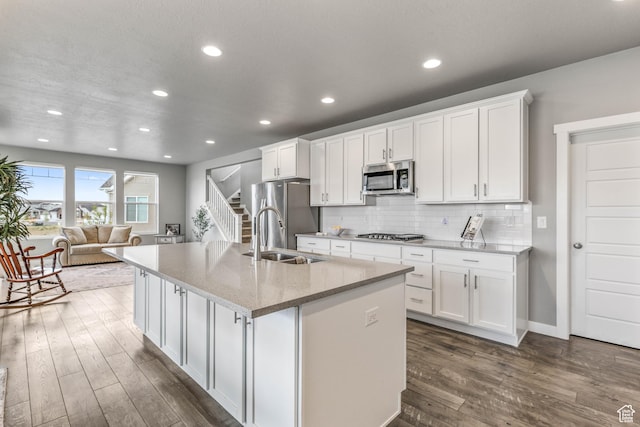 kitchen with white cabinets, a sink, appliances with stainless steel finishes, dark wood finished floors, and an island with sink