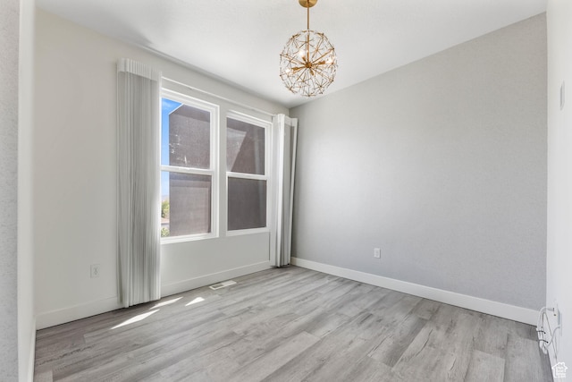 empty room featuring light wood finished floors, a chandelier, and baseboards