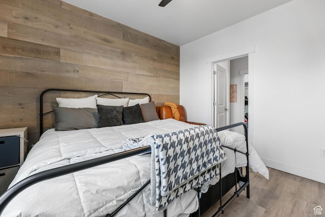 bedroom with wood walls, wood finished floors, baseboards, and ceiling fan