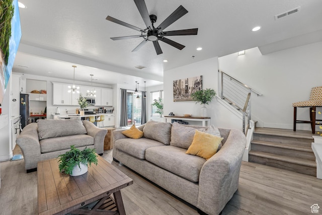 living room with stairs, a chandelier, light wood finished floors, ceiling fan, and recessed lighting
