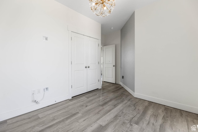 empty room with wood finished floors, a chandelier, and baseboards
