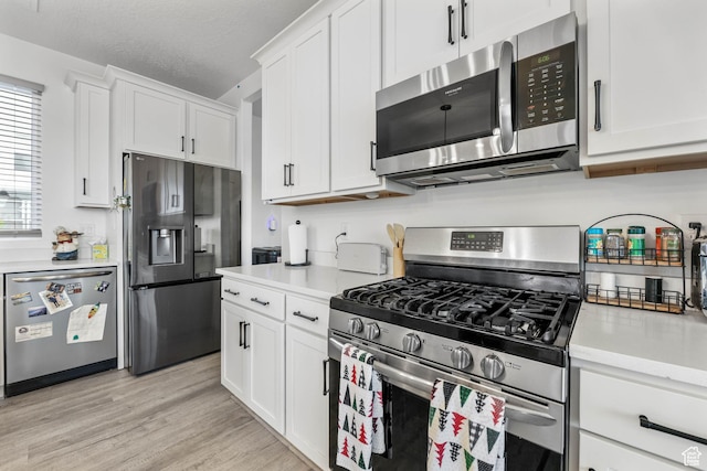 kitchen with appliances with stainless steel finishes, light countertops, white cabinetry, and light wood-style floors