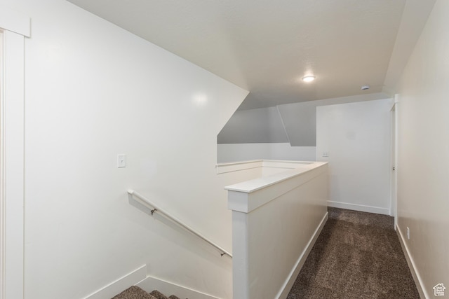 hallway with an upstairs landing, baseboards, and dark carpet