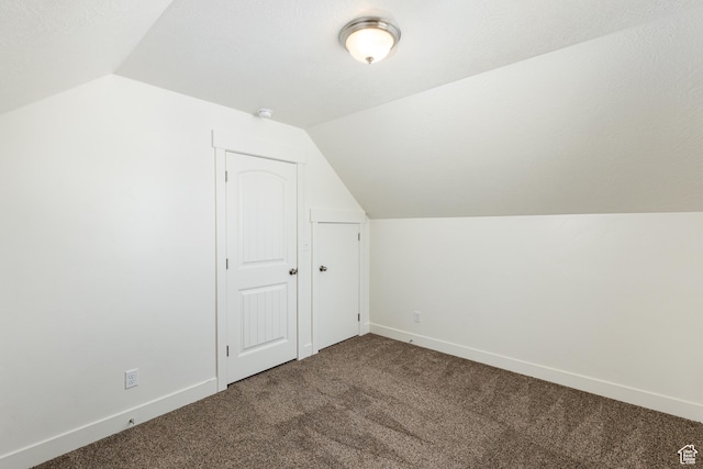 additional living space with vaulted ceiling, dark colored carpet, and baseboards