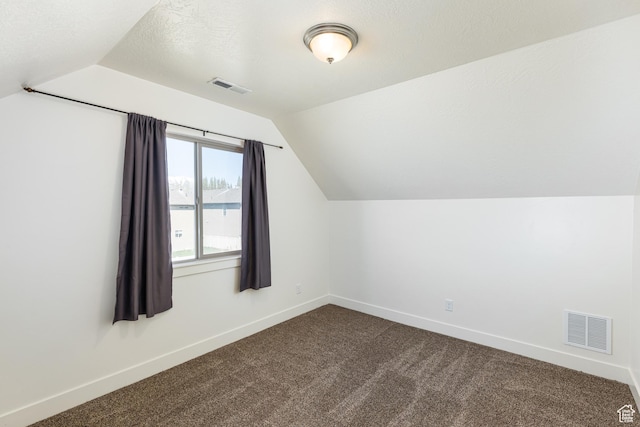 additional living space with dark colored carpet, visible vents, and vaulted ceiling
