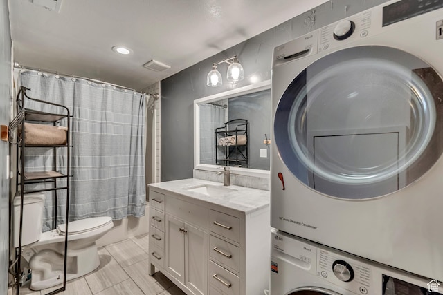 bathroom featuring stacked washing maching and dryer, toilet, curtained shower, vanity, and visible vents