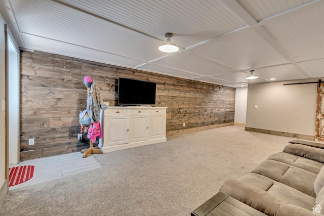 unfurnished living room with a barn door, wood walls, light colored carpet, and baseboards