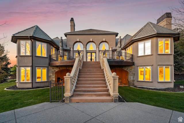 1714 Ridge Point Dr, Bountiful, UT 84010 - back of property at dusk featuring a balcony, a yard, stucco siding, and a chimney