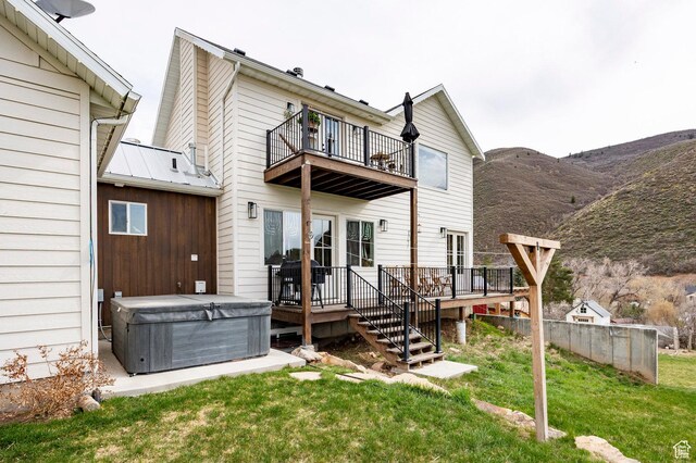 rear view of house featuring a hot tub, a deck with mountain view, a yard, and a balcony