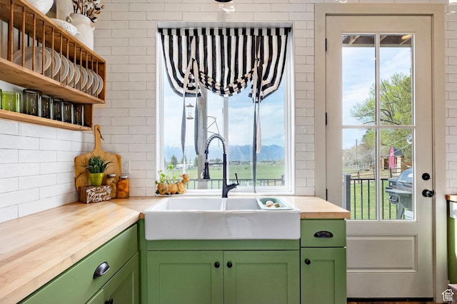 kitchen with a sink, green cabinetry, open shelves, and butcher block countertops