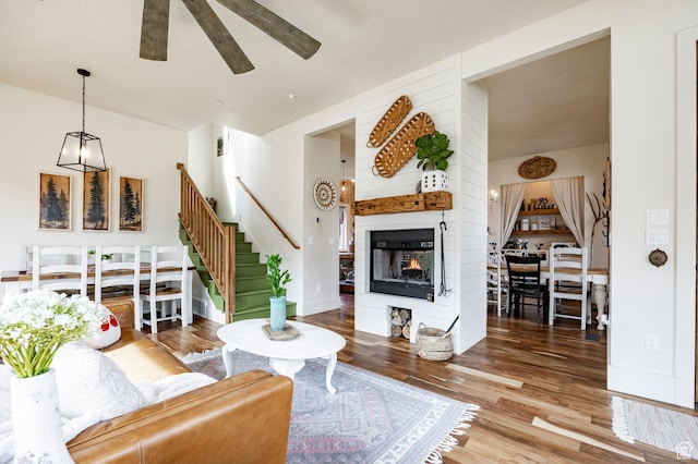 living area featuring a ceiling fan, a multi sided fireplace, wood finished floors, and stairway