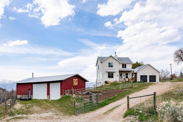view of front of home with fence, a garage, dirt driveway, an outbuilding, and a chimney