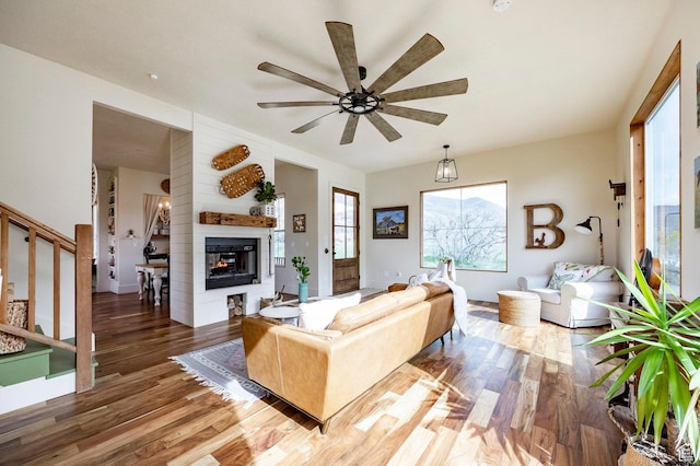 living room featuring stairs, a ceiling fan, a glass covered fireplace, and wood finished floors