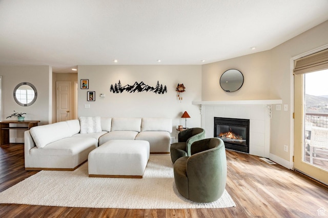 living room with wood finished floors, a tiled fireplace, and recessed lighting