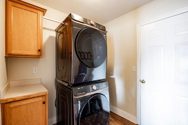 washroom with dark wood-style floors, cabinet space, stacked washer and clothes dryer, and baseboards