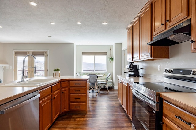kitchen with brown cabinets, a sink, stainless steel appliances, under cabinet range hood, and dark wood-style flooring