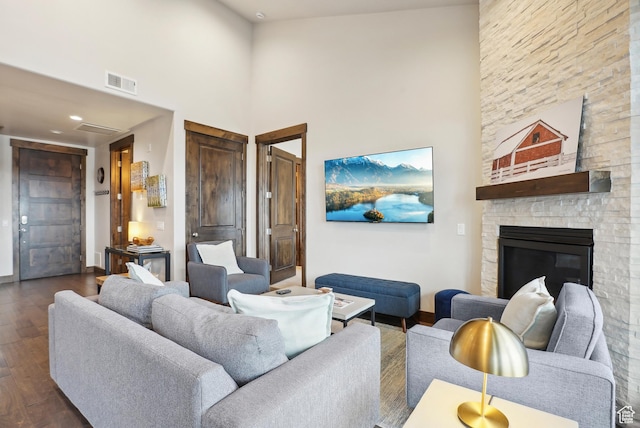 living area featuring dark wood-style flooring, a fireplace, visible vents, baseboards, and a towering ceiling