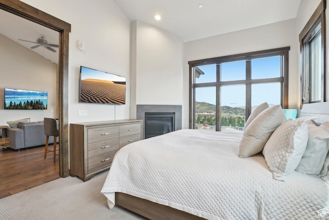 bedroom featuring a glass covered fireplace, recessed lighting, wood finished floors, and vaulted ceiling