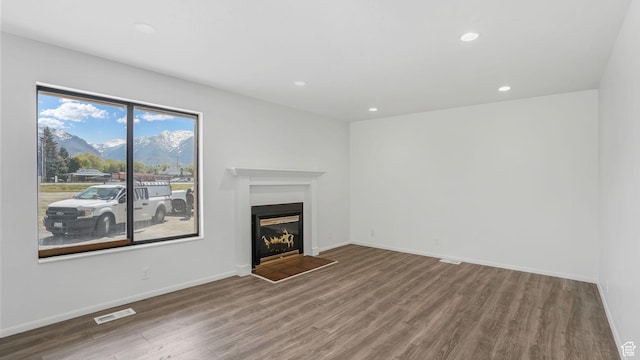 unfurnished living room with recessed lighting, wood finished floors, a mountain view, a glass covered fireplace, and visible vents