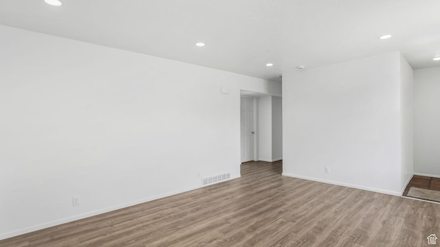 empty room featuring wood finished floors, visible vents, recessed lighting, and baseboards