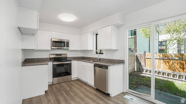 kitchen with white cabinets, a sink, visible vents, stainless steel appliances, and wood finished floors