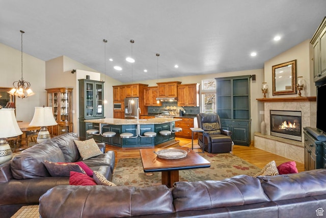 living area featuring light wood finished floors, recessed lighting, a tiled fireplace, a notable chandelier, and lofted ceiling