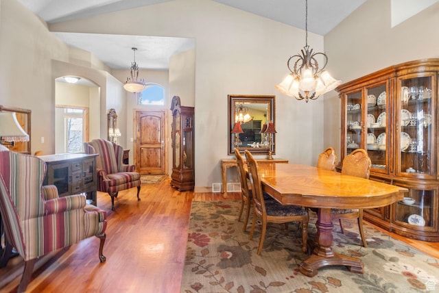 dining area with a chandelier, high vaulted ceiling, light wood finished floors, and arched walkways
