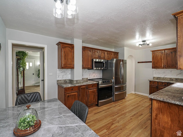 123 Lynnwood Dr, Clearfield, UT 84015 - kitchen featuring arched walkways, appliances with stainless steel finishes, backsplash, light wood finished floors, and a textured ceiling