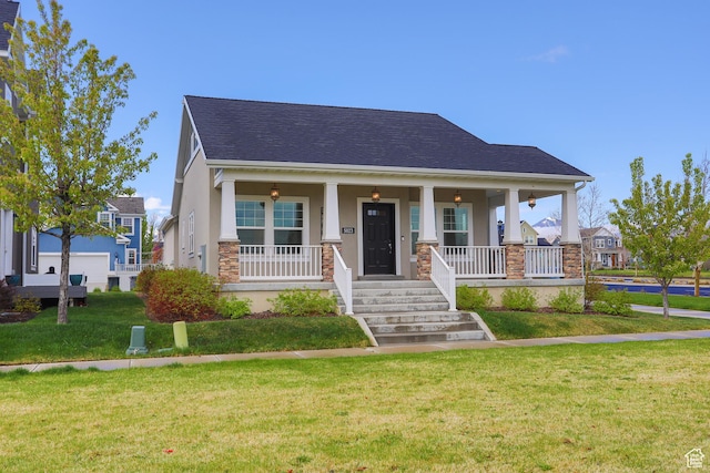 view of front of house featuring stone siding, roof with shingles, covered porch, a front yard, and stucco siding