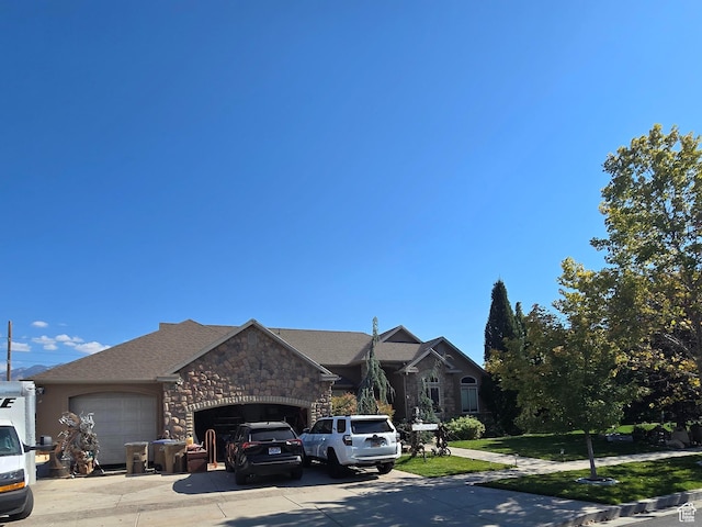 view of front of house with stone siding, driveway, a front lawn, and a garage
