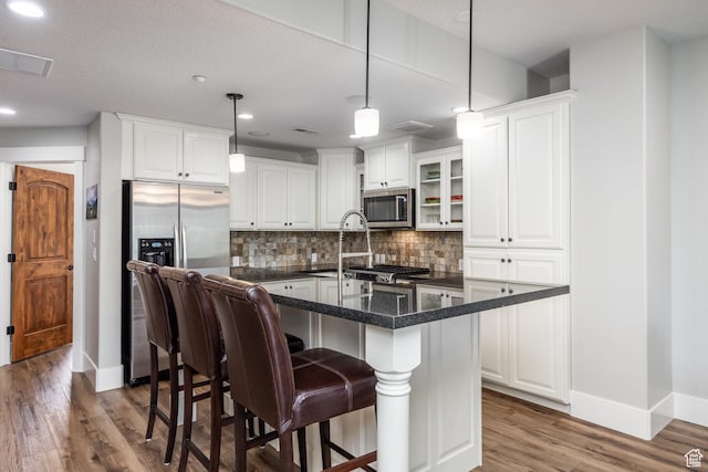 13386 N Alexis Dr, Kamas, UT 84036 - kitchen with appliances with stainless steel finishes, wood finished floors, decorative backsplash, white cabinets, and a kitchen bar