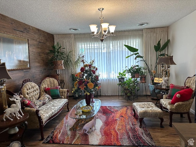 living room featuring a textured ceiling, wood walls, visible vents, an inviting chandelier, and wood finished floors