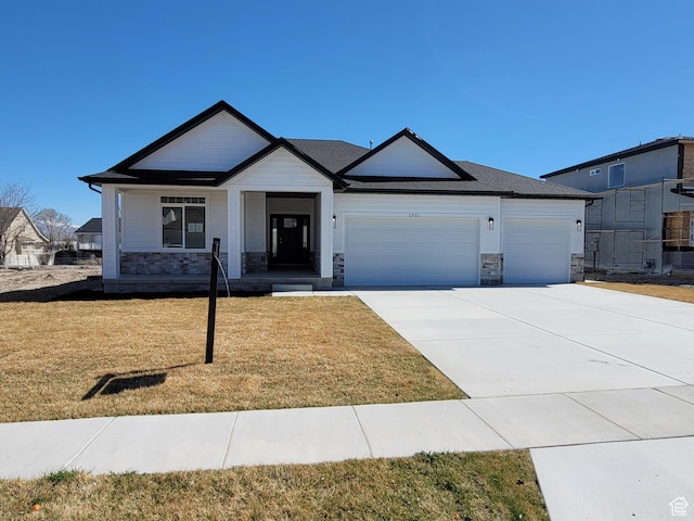 view of front facade with a front yard, stone siding, an attached garage, and concrete driveway