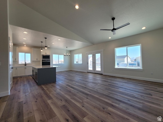 unfurnished living room featuring baseboards, recessed lighting, vaulted ceiling, ceiling fan with notable chandelier, and dark wood-style floors