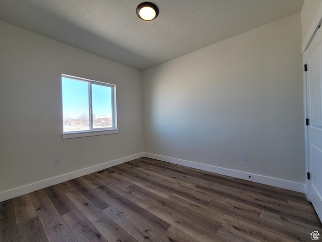 unfurnished room featuring dark wood-style flooring, visible vents, and baseboards
