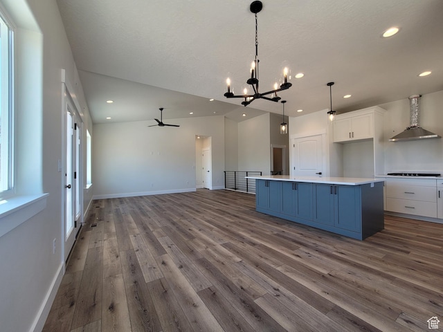 kitchen with wood finished floors, blue cabinetry, wall chimney range hood, white cabinets, and black stovetop