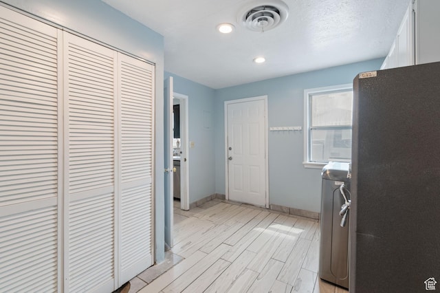 kitchen featuring visible vents, freestanding refrigerator, washer and dryer, baseboards, and white cabinetry