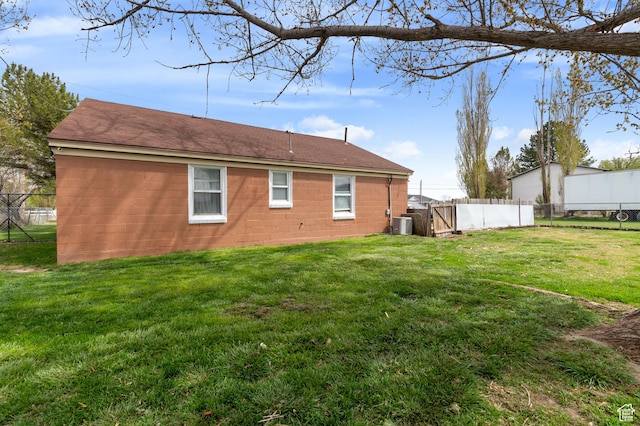 rear view of house with a lawn, a shingled roof, concrete block siding, and fence
