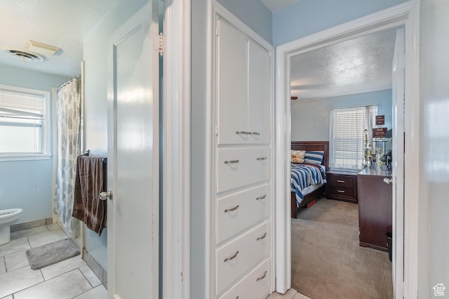 hall featuring a textured ceiling, visible vents, and a wealth of natural light