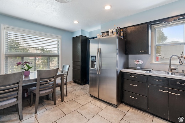 kitchen featuring dark cabinets, light countertops, light tile patterned floors, a sink, and stainless steel fridge