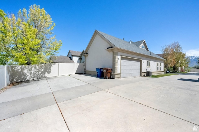 6872 S Triumph Ln, West Jordan, UT 84088 - view of side of property featuring concrete driveway, stucco siding, an attached garage, and roof with shingles