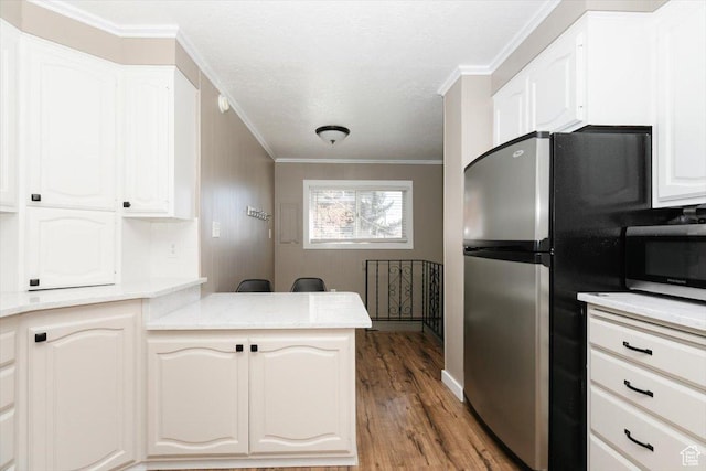 kitchen featuring crown molding, white cabinets, light countertops, stainless steel appliances, and wood finished floors