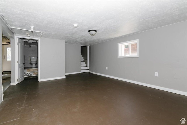 basement featuring baseboards, a textured ceiling, and stairway